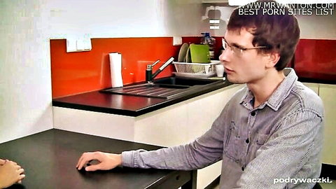 Young brunette guy with glasses leaning on kitchen table in casual shirt