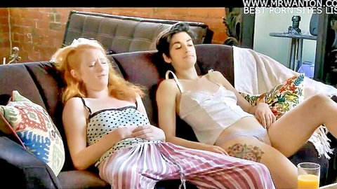 Freckled redhead pulls pink pants down exposing shaved pussy lounging with spread-leg brunette in white lingerie on couch