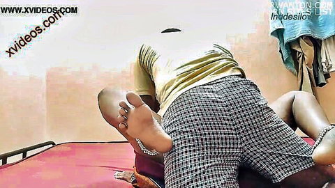 Desi woman in plaid shorts behind bent-over guy on red bed feet with anklets homemade Indian couple
