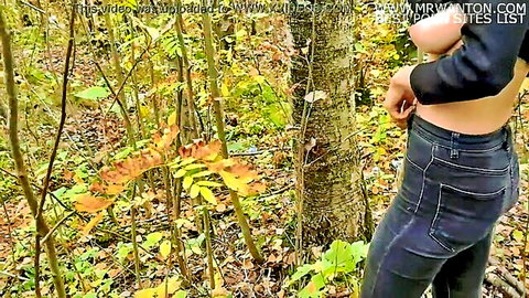 Slim woman in jeans and crop top posing in autumn woods