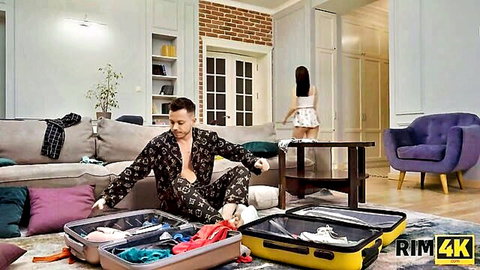 Bearded man in open pajamas unpacks lingerie suitcases while sexy Russian teen in mini skirt and stockings stands nearby