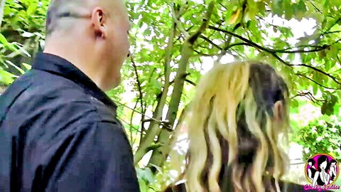 Bald man in black shirt embraces busty blonde MILF outdoors in green park