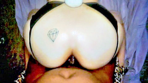 Busty pale woman with diamond tattoo squeezes massive tits around white ball in black harness cleavage