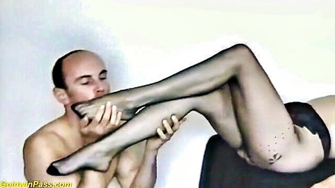 Bald man worshipping woman's stockinged feet and legs in black lingerie