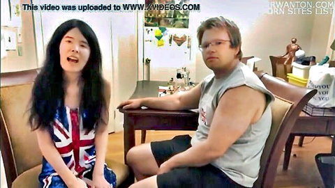Busty Asian teen in skimpy Union Jack dress flashes deep cleavage teasing geeky white guy on couch