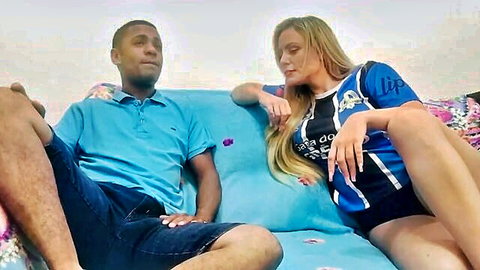 Blonde woman in sports jersey flirts with black man on couch, casual intimate moment