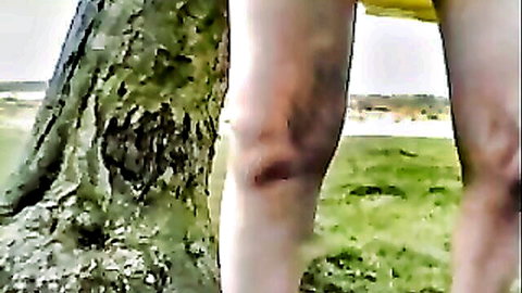 Secretary Gisela in short yellow skirt outdoors, legs exposed by tree