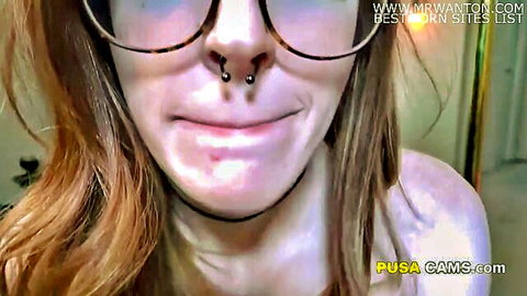 Closeup of smirking redhead camgirl with glasses, septum piercing and long hair