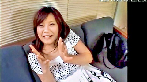 Smiling Japanese mature woman in polka dot dress gesturing on couch