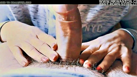 Red-nailed hands gripping and stroking a thick erect cock in close-up handjob.