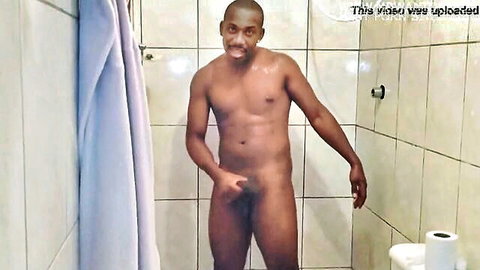 Muscular black man naked in shower, smiling and posing with hand on erect penis