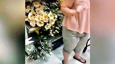 Mature granny in pink top and gray pants browsing flowers in store