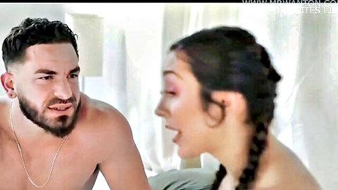 Muscular shirtless Latino guy with beard stares intensely at smiling braided brunette babe close-up on bed
