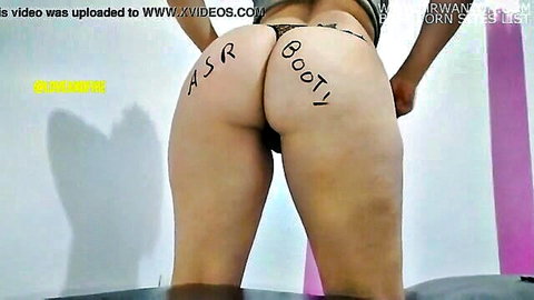 Curvy woman squatting in black thong, big ass with 'ASS BOOTY' written during naked workout