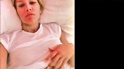 Charissa Thompson lying in bed wearing white t-shirt, blonde beauty solo