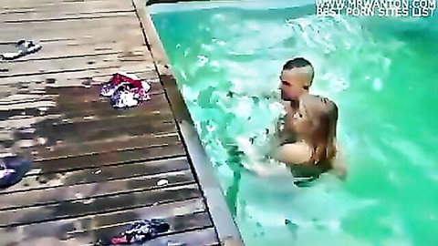 Muscular shaved-head guy passionately embraces wet blonde babe in turquoise pool water