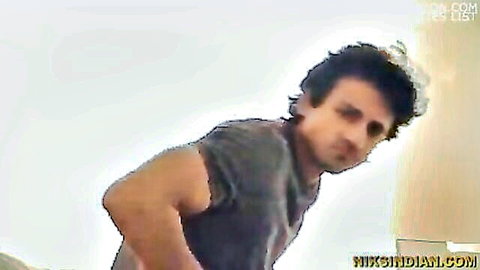 Indian man in gray tank top leaning forward with intense expression