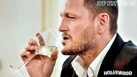 Bearded handsome man in black suit sips white wine sensually closeup