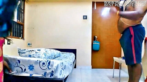 Chubby Indian man in red shorts standing by bed exposing belly in amateur bedroom