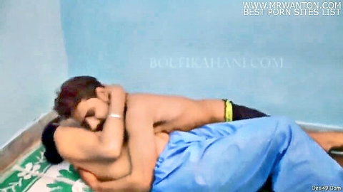 Shirtless Indian man passionately hugs curvy brunette nurse in blue scrubs from behind on mat