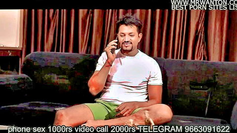 South Asian man in white t-shirt and green shorts sits on couch talking on phone sex call