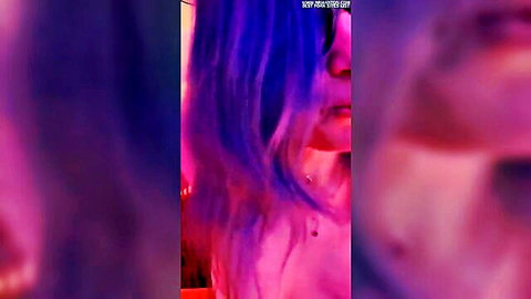 Blurry close-up of purple-haired woman with piercings in dim purple lighting, BDSM vibe