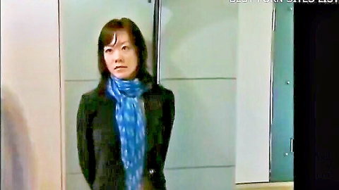 Brunette East Asian MILF in black coat and blue scarf standing in hotel hallway