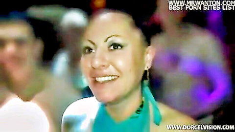 Smiling brunette with hoop earrings in dimly lit group sex party scene