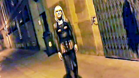 Petite blonde in revealing black latex outfit posing seductively in dark urban alley at night