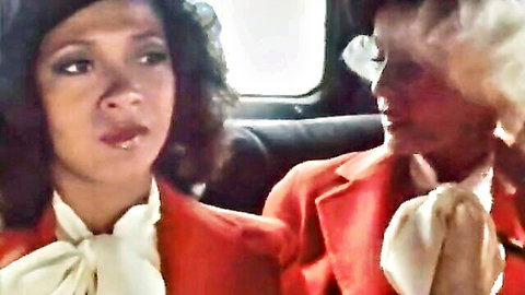 Seka and curly-haired woman in red blazers, intense gaze in vintage 1980 adult scene