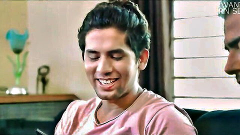 Smiling South Asian man in pink t-shirt with male friend in cozy Indian room