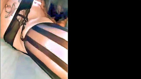 Closeup of tattooed woman's thigh in shiny black striped stockings and lace garter teasing crotch