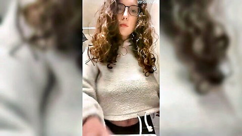 Curly-haired girl with glasses teases in cropped hoodie showing midriff