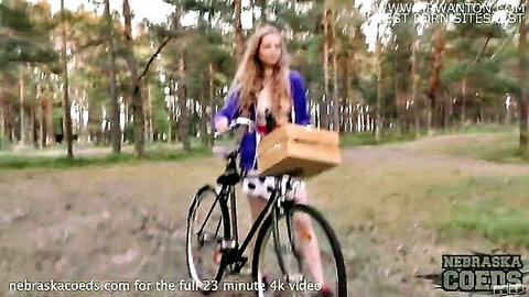 Skinny blonde babe rides bicycle in forest wearing short skirt and open top teasing perky tits