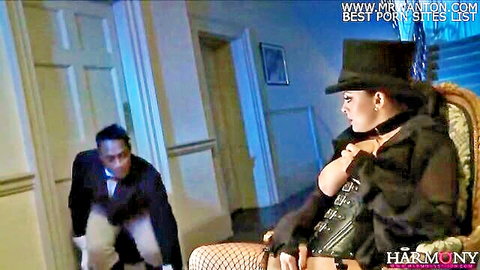 Liza in black corset and top hat with suited black man peeking