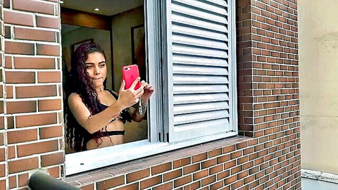 Sexy young Latina brunette with tattoos in black bralette takes voyeur selfie from window