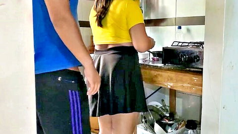 Latina woman in yellow crop top and short black skirt cooking with step-brother-in-law behind her