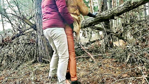 Clothed woman in pink jacket hugging furry orangutan against tree in forest