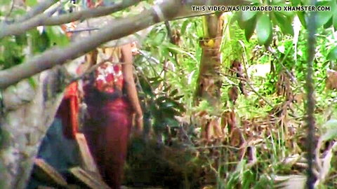 Sexy South Asian woman in tight red top and pants posing in lush jungle foliage