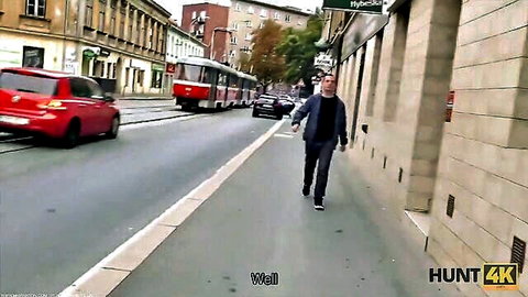 Man in dark jacket and jeans walks confidently on city sidewalk past red tram and car in Hunt4K series