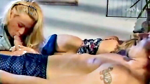 Blonde woman in denim jacket kisses shirtless man's bulging cock through blue boxers on couch