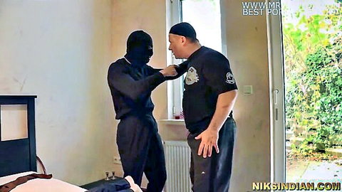 Masked Indian man in black grabs muscular guy's arm in tense bedroom standoff