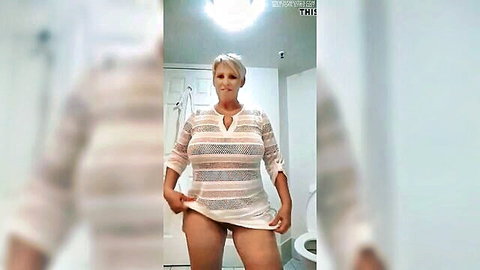 Mature blonde MILF lifts sheer striped dress flashing shaved pussy and huge tits in bathroom