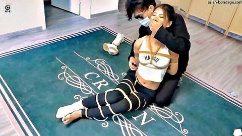 Asian woman tied up and gagged in BDSM scene with masked man