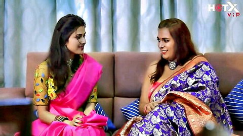 Two sexy Indian women in tight sarees sitting on couch smiling seductively