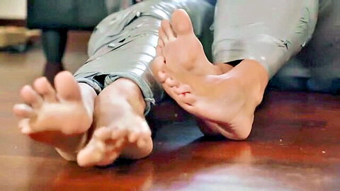 Bare feet with toes spread and legs bound in shiny gray tape on wooden floor in foot bondage fetish