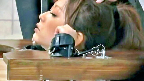Japanese woman locked in wooden pillory with handcuffs and blindfold for intense BDSM bondage