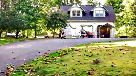 Outdoor suburban house with open garage and red scooter parked in driveway surrounded by green trees and grass