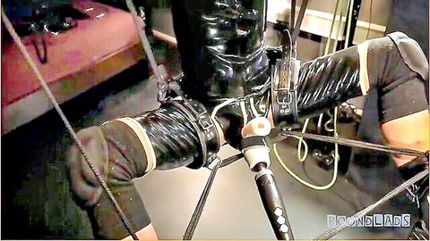 Suspended male gimp in black latex bondage with dildo, gay BDSM fetish