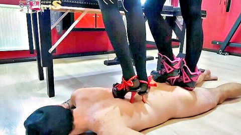 Three women in stockings and heels trampling naked bound man in BDSM torture